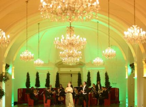 Das Schloss Schönbrunn Orchester spielt in der Orangerie Schönbrunn ein klassisches Konzert. Im Vordergrund sieht man die Sängerin, die die Konzerte begleitet.