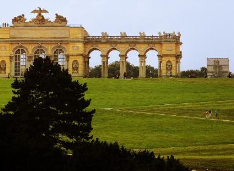 Die berühmte Gloriette des Schloss Schönbrunn, man sieht den linken Teil des Gebäudes und den Mittelteil, davor der kleine Berg auf den einige Touristen hinaufgehen