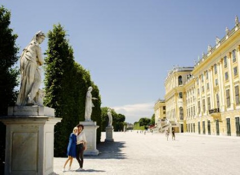 Die Touristenattraktion Schloss Schönbrunn in Wien, man sieht rechts das Schloss und links zwei Touristen die ein Foto im Garten machen
